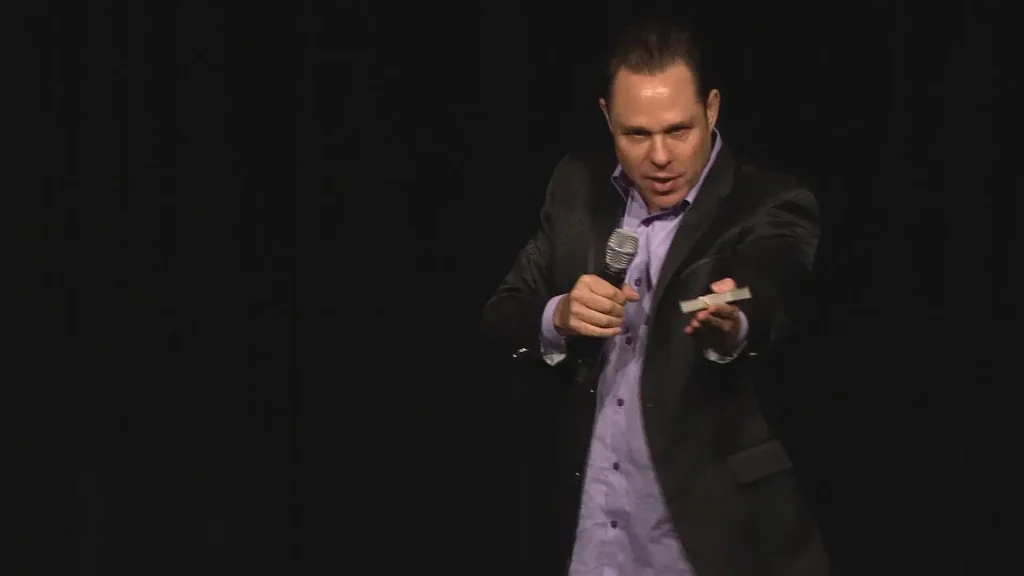 Randy Charach with holding mic and performing on stage.